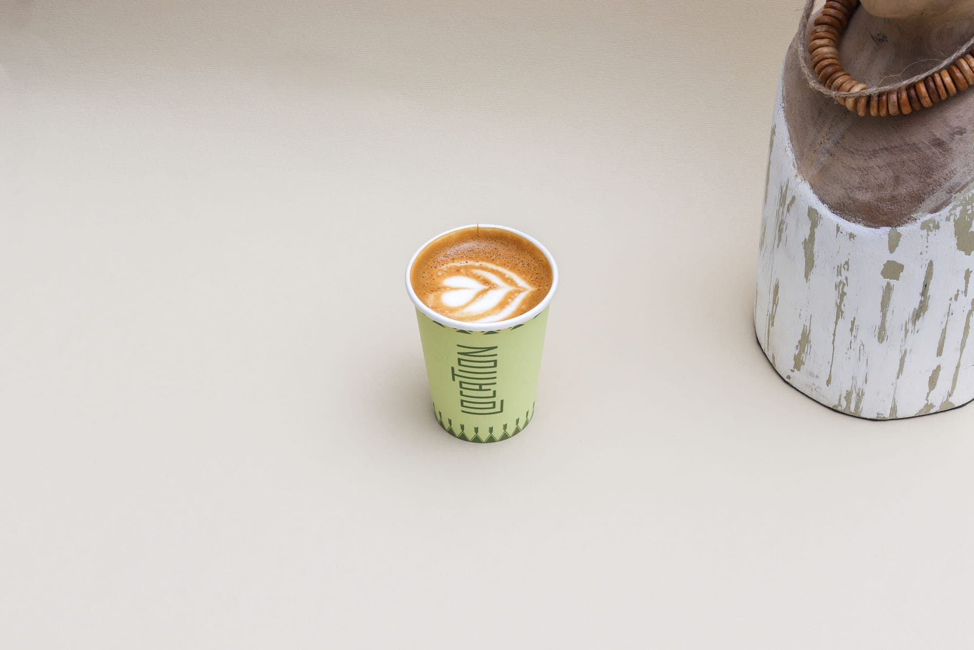 Location paper cup with latte art beside a weathered wooden jar